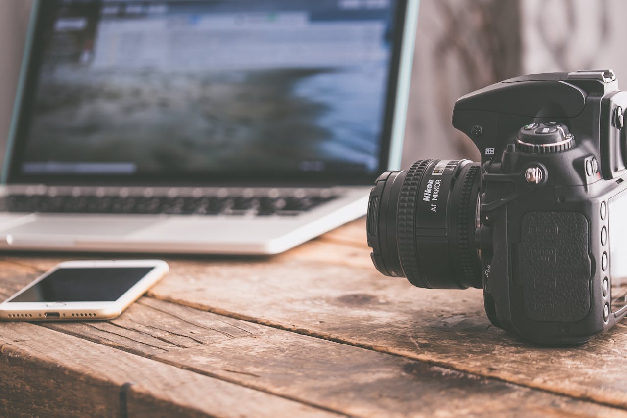 Crafting Captivating Headlines: Your awesome post title goes here Close-up of a DSLR camera, laptop, and smartphone on a wooden table in a modern workspace.